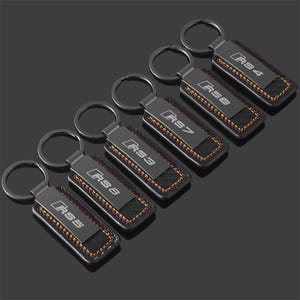 May include: Six black keyrings with silver hoops. Each keyring has a black rectangular plate with "RS" followed by a number, and a carbon fibre-style insert with red and yellow stitching.