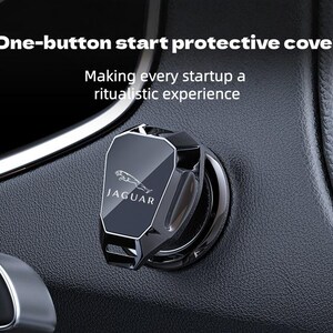 May include: A black, angular protective cover for a car's one-button start ignition, featuring the Jaguar logo and text. The cover is mounted on a textured black dashboard surface. Text on the image reads: One-button start protective cover.