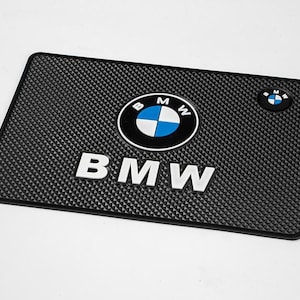 Peut inclure: Un tapis de bar rectangulaire en caoutchouc noir avec une surface texturée à motif diamant. Le tapis présente le logo BMW blanc, bleu et noir au centre, le texte BMW en blanc en dessous et un plus petit logo BMW circulaire en haut à droite.