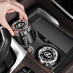 Puede incluir: Dos ambientadores de coche cilíndricos negros con tapas metálicas plateadas en forma de ventilador que muestran el logotipo de Lexus. El lateral de la unidad muestra el texto CAR AIR PAMTI CA. Estos dispositivos encajan en portavasos estándar.