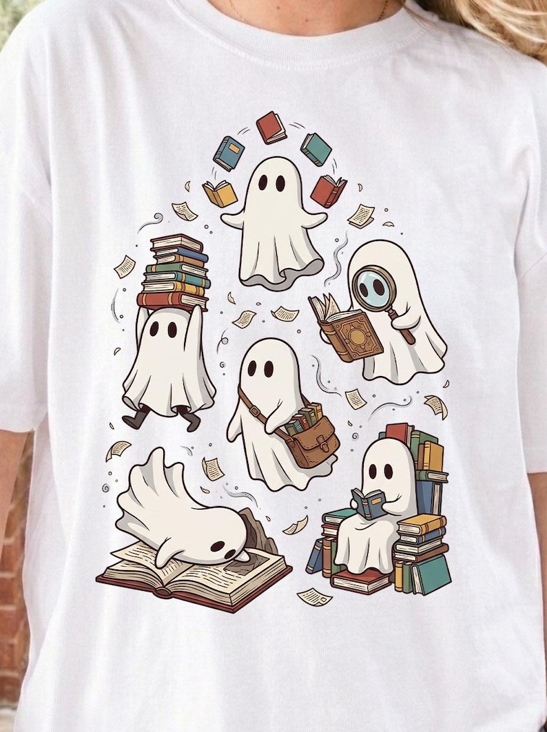 May include: A white t-shirt featuring a graphic illustration of five white ghosts interacting with books. One ghost juggles books, one uses a magnifying glass, one carries a satchel, one rests on an open book, and one sits on a stack of books.