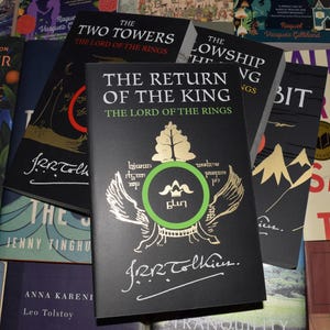 May include: A collection of hardcover books from "The Lord of the Rings" series. The books have black covers with gold and green accents. The title "The Return of the King" is prominently displayed on the front cover, along with the author's signature.