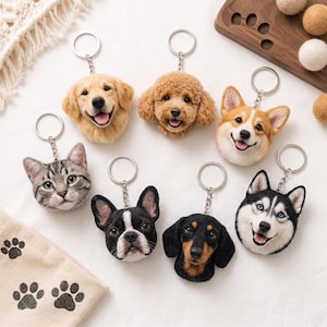 Peut inclure: Un ensemble de sept porte-clés en feutre représentant des têtes d'animaux : un golden retriever, un caniche, un corgi, un chat tigré, un bouledogue français, un teckel et un husky, chacun fixé à un anneau brisé en métal argenté.