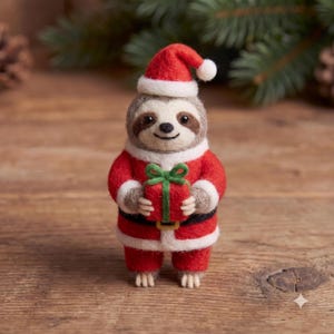 Könnte beinhalten: Eine aus Nadelfilz gefertigte Faultier-Figur, die einen rot-weißen Weihnachtsmannanzug mit passender Mütze trägt. Das Faultier hat braune Gesichtszeichnungen, schwarze Augen und ein kleines Lächeln. Es hält ein rotes Geschenk mit grüner Schleife.