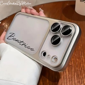 Könnte beinhalten: Silberfarbene Handyhülle mit durchsichtigem Rücken und dem Namen "Beatrice" in schwarzer Schrift. Die Hülle hat ein Kameramodul mit drei Linsen und einem Blitz. In der oberen linken Ecke der Hülle steht der Text "Case Studio By Meloo".