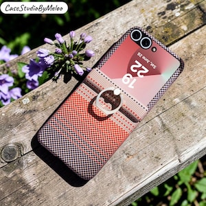 May include: A phone case with a ring holder, featuring a red and black checkered pattern and a beige and red striped design. The phone screen shows the date and time. The case is designed to fit a mobile phone.