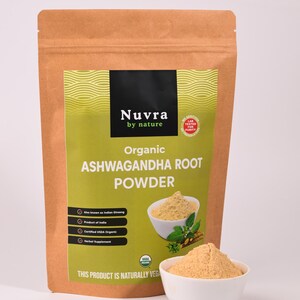 May include: A brown paper bag of organic Ashwagandha root powder with a green and black label. The label includes the text "Nuvra by nature" and "Organic Ashwagandha Root Powder". A small white bowl of powder is in front of the bag.