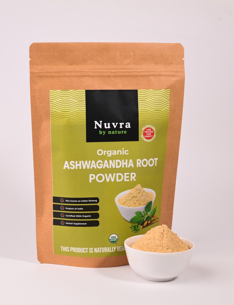 May include: A brown paper bag of organic Ashwagandha root powder with a green and black label. The label includes the text "Nuvra by nature" and "Organic Ashwagandha Root Powder". A small white bowl of powder is in front of the bag.