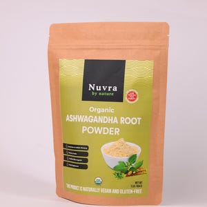May include: A brown paper bag of Nuvra Organic Ashwagandha Root Powder. The bag has a green and yellow label with the product name and a picture of the powder in a white bowl with green leaves. The text on the bag says the product is naturally vegan and gluten-free.