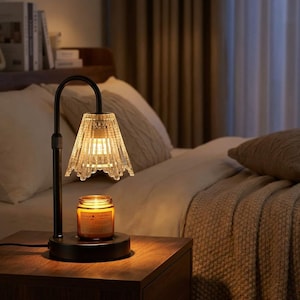 Puede incluir: Lámpara de noche de metal negro con una pantalla de cristal transparente texturizado y un calentador de velas. La lámpara está sobre una mesita de noche de madera en un dormitorio. El calentador de velas es un tarro de cristal con una etiqueta.