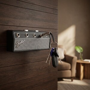 Puede incluir: Un llavero negro y plateado con forma de amplificador Fender montado en una pared de madera oscura. El llavero tiene un dise&ntilde;o de rejilla de altavoz y el logotipo de Fender. Un juego de llaves cuelga del llavero.