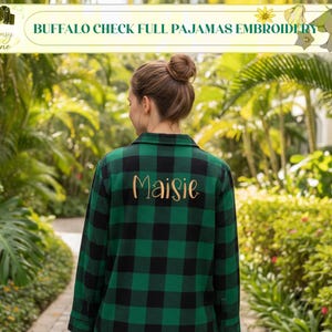 May include: A green and black buffalo check pajama shirt with the name "Maisie" embroidered in gold thread. The shirt is part of a set and is displayed outdoors with lush greenery in the background. The top banner reads "BUFFALO CHECK FULL PAJAMAS EMBROIDERY".