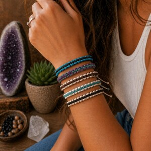 May include: A stack of five woven cord bracelets featuring various color combinations including turquoise, black, brown, and purple. Each bracelet is constructed with a knotted pattern and includes adjustable pull strings with small beads at the ends.