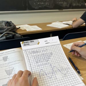 K&ouml;nnte beinhalten: Ein wei&szlig;es Notizbuch mit Millimeterpapier und der &Uuml;berschrift GRAPH/GRID NOTES, das handschriftliche Analysis-Gleichungen und einen gezeichneten Sinuskurven-Graphen enth&auml;lt. Es liegt auf einem Holztisch neben einem Lehrbuch und zwei Druckbleistiften.