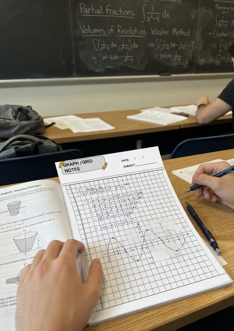 K&ouml;nnte beinhalten: Ein wei&szlig;es Notizbuch mit Millimeterpapier und der &Uuml;berschrift GRAPH/GRID NOTES, das handschriftliche Analysis-Gleichungen und einen gezeichneten Sinuskurven-Graphen enth&auml;lt. Es liegt auf einem Holztisch neben einem Lehrbuch und zwei Druckbleistiften.