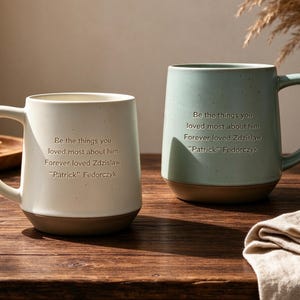 May include: Two ceramic mugs with speckled finishes, one cream and one sage green. Each mug features the engraved text: Be the things you loved most about him. Forever loved Zdzislaw "Patrick" Fedorczyk. Both mugs have a solid brown base.