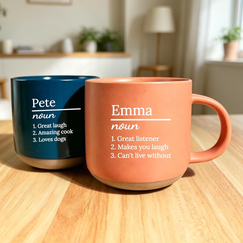 May include: Two ceramic mugs, one navy blue and one coral, with white text. The navy mug says "Pete" and lists qualities. The coral mug says "Emma" and lists qualities. Both mugs have a rounded base and a handle.