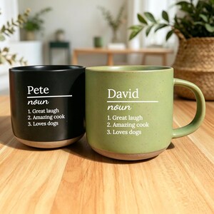 May include: Two ceramic mugs, one black and one green, with the names "Pete" and "David" printed in white. Each mug has a list of three qualities: "Great laugh," "Amazing cook," and "Loves dogs."
