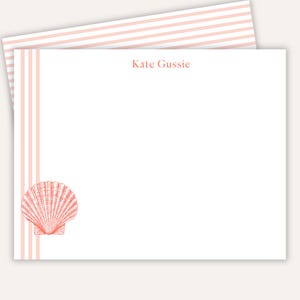 May include: A white rectangular stationery card featuring the name Kate Gussie printed in coral pink. The left side displays vertical coral pink stripes and a detailed coral pink seashell illustration. The top edge shows a matching striped pattern.