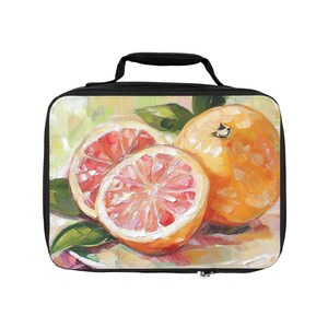 Op de afbeelding: Een rechthoekige lunchtas met een zwart handvat en rits, voorzien van een olieverfschilderij-print van een hele sinaasappel en twee doorgesneden grapefruithelften met roze binnenkant en groene bladeren op een geel-groene achtergrond.