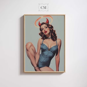 Op de afbeelding: Ingelijste kunstwerk met een vrouw in een tealkleurig badpak, rode hoorns en een halo. Het kunstwerk heeft een vintage pin-up stijl met een lichtblauwe achtergrond. De lijst heeft een lichte houtkleur. De afbeelding heeft de letters "CM" in de bovenhoek.