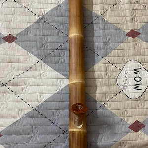 Può includere: Una pipa ad acqua alta e cilindrica in bambù con finitura marrone. Presenta una ciotola e un bocchino. Il bambù ha segni naturali ed è posto su uno sfondo a motivi.