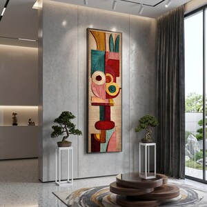 Könnte beinhalten: Abstrakte Wandkunst mit einem geometrischen Design in Rot, Türkis, Gelb und Rosa. Das Kunstwerk ist gerahmt und auf einem hellen Hintergrund montiert. Zwei Bonsai-Bäume stehen auf weißen Ständern, und ein Holztisch mit einem runden Teppich befindet sich im Vordergrund.