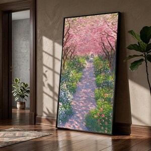 以下が含まれることがあります： 鮮やかなピンク色の花を咲かせた木々に囲まれた庭の小道を写した、額入りのアートプリント。小道は日陰になっており、木漏れ日が降り注いでいます。緑豊かな草木と色とりどりの花が小道の両側に並び、穏やかで魅力的な風景を作り出しています。