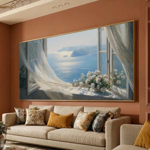 May include: A large framed painting depicts a coastal scene with an open window. White curtains billow in the breeze, revealing a bright blue sea and sky. White flowers sit on the windowsill. A beige sofa with decorative pillows is in front of the painting.