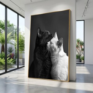 Puede incluir: Impresión enmarcada en blanco y negro de dos gatos abrazándose. Uno es negro, el otro blanco, en un marco dorado. La obra de arte se exhibe en una habitación luminosa y moderna con ventanas.