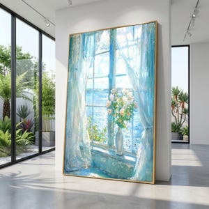 May include: A framed painting of a window scene with blue curtains and a sea view. A vase of white flowers sits on the windowsill. The artwork has a gold frame and is displayed in a modern, well-lit space.