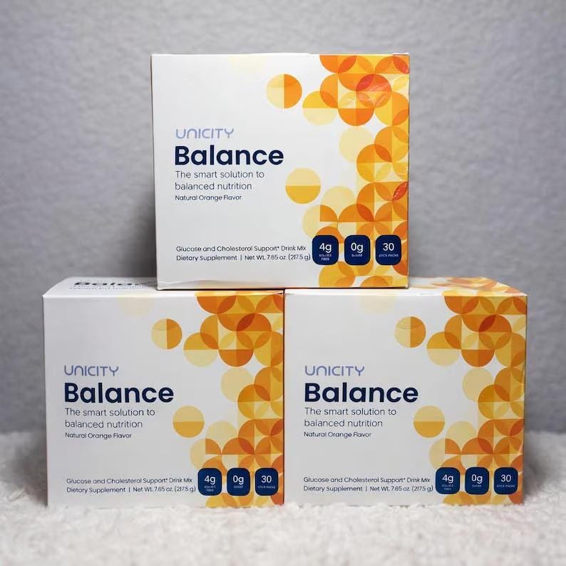 May include: Three white boxes of Unicity Balance dietary supplement. Each box features the product name and description in blue and orange text. The boxes have an orange geometric design on the right side. Each box contains 275 g.
