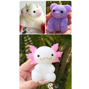 May include: Three small figurines featuring a white hamster with pink cheeks, a textured purple bear with black eyes, and a white axolotl with pink gills and a black stitched mouth. Each image includes the logo Salty Kaitlin LLC Cape Coral, Florida.