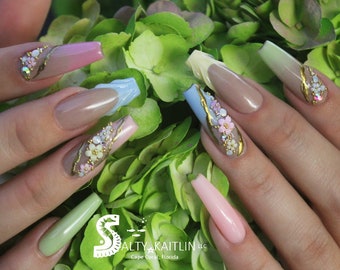 May include: Long, almond-shaped nails with a gradient design in shades of pink, blue, and green. Each nail is decorated with gold accents and small, delicate flowers.