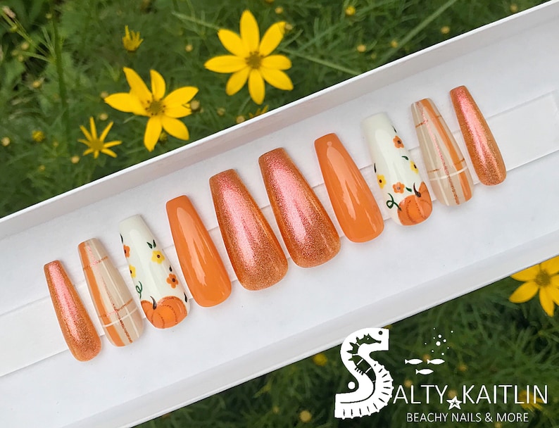 Peut inclure: Ensemble de dix faux ongles longs, orange et blanc sur le th&egrave;me de l'automne. Les ongles pr&eacute;sentent des motifs de citrouille, de carreaux et de fleurs.