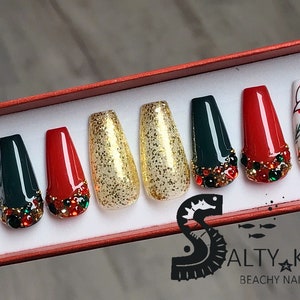 Puede incluir: Conjunto de diez u&ntilde;as postizas con tem&aacute;tica navide&ntilde;a. Las u&ntilde;as est&aacute;n decoradas con purpurina dorada, pedrer&iacute;a roja y verde, acebo verde y blanco y bayas rojas.