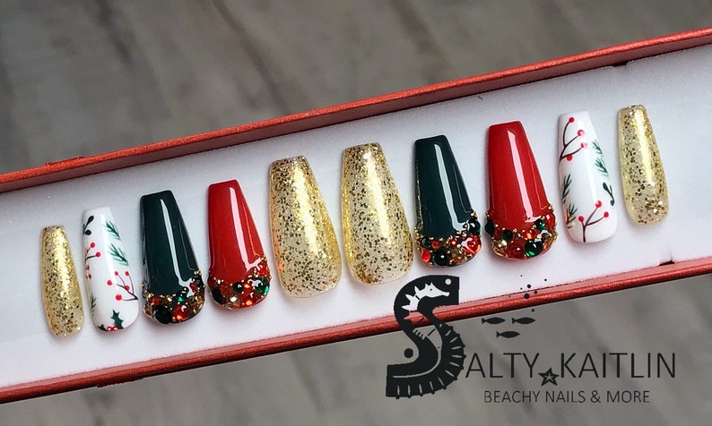 Puede incluir: Conjunto de diez u&ntilde;as postizas con tem&aacute;tica navide&ntilde;a. Las u&ntilde;as est&aacute;n decoradas con purpurina dorada, pedrer&iacute;a roja y verde, acebo verde y blanco y bayas rojas.