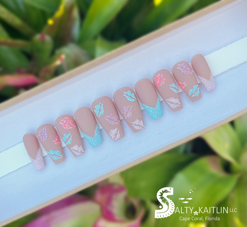 May include: Set of ten nude-colored press-on nails with a light blue glitter accent and pink and blue glitter butterfly designs. The nails are displayed in a white box with the text "Salty Kaitlin LLC Cape Coral, Florida".