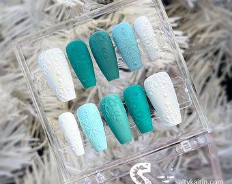 May include: A set of ten false nails in a clear plastic box. The nails are a gradient of blue and green colors with a snowflake design. The nails are in a coffin shape.