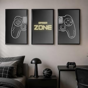 Könnte beinhalten: Drei gerahmte schwarze Wandkunstwerke mit weißen Controller-Umrissen und dem Text "GAMER ZONE" in einer Schriftart im Neon-Stil. Der Raum verfügt über einen schwarzen Schreibtisch, ein Bett mit grauer Bettwäsche und einen schwarzen Nachttisch mit einer Lampe und einem Basketball.