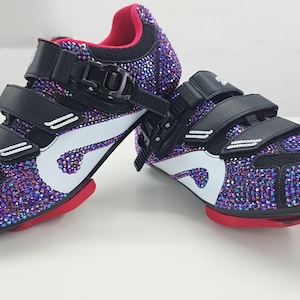 May include: A pair of cycling shoes covered in iridescent purple rhinestones. The shoes have black straps and accents, a white logo, and red soles. The interior is pink.