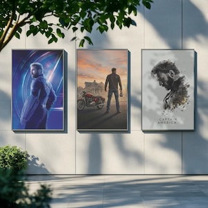 May include: Three framed art prints displayed outdoors. The prints feature images of a superhero in a blue and purple setting, a man with a motorcycle, and a portrait with the text "CAPTAIN AMERICA".