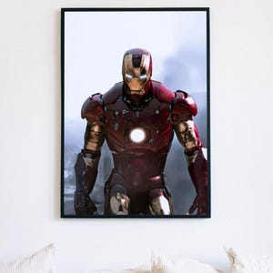K&ouml;nnte beinhalten: Gerahmter Druck von Iron Man in seiner rot-goldenen R&uuml;stung, der vor einem verschwommenen Hintergrund steht. Das Kunstwerk zeigt den ikonischen Helm und das Brustst&uuml;ck des Superhelden mit leuchtenden Lichtern. Der Druck ist in einem schwarzen Rahmen.