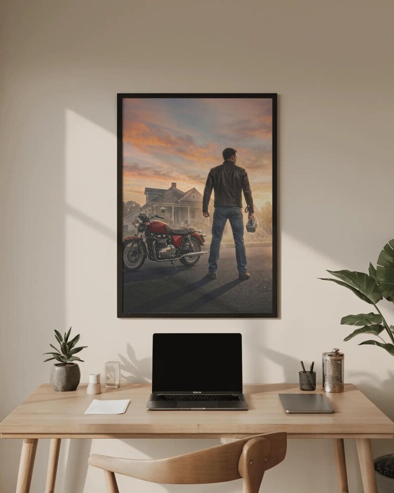 May include: Framed print of a man standing in front of a red motorcycle and a house at sunset. The man is wearing a leather jacket and jeans, holding a helmet. The motorcycle is parked on a road.