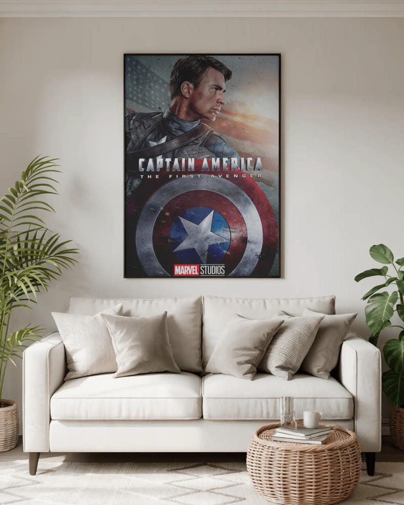 Może przedstawiać: Oprawiony plakat z filmu Kapitan Ameryka: Pierwsze starcie, przedstawiający postać w bohaterskiej pozie. Plakat ma czarną ramę i jest wyświetlany nad białą sofą z beżowymi poduszkami. Widoczne jest logo Marvel Studios.