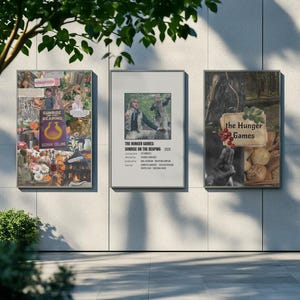 May include: Three framed posters, each with imagery from "The Hunger Games". The central poster reads "The Hunger Games: Sunrise on the Reaping 2025". The left poster displays "Sunrise Reaping" and "Suzanne Collins". The right poster has the text "the Hunger Games".