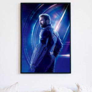 May include: Framed print featuring Captain America in a blue and black suit, holding his shield. The background has a blue and purple gradient with the Avengers logo. The image is in a black frame.