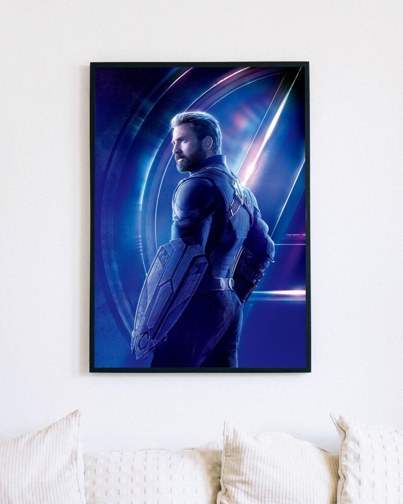 May include: Framed print featuring Captain America in a blue and black suit, holding his shield. The background has a blue and purple gradient with the Avengers logo. The image is in a black frame.