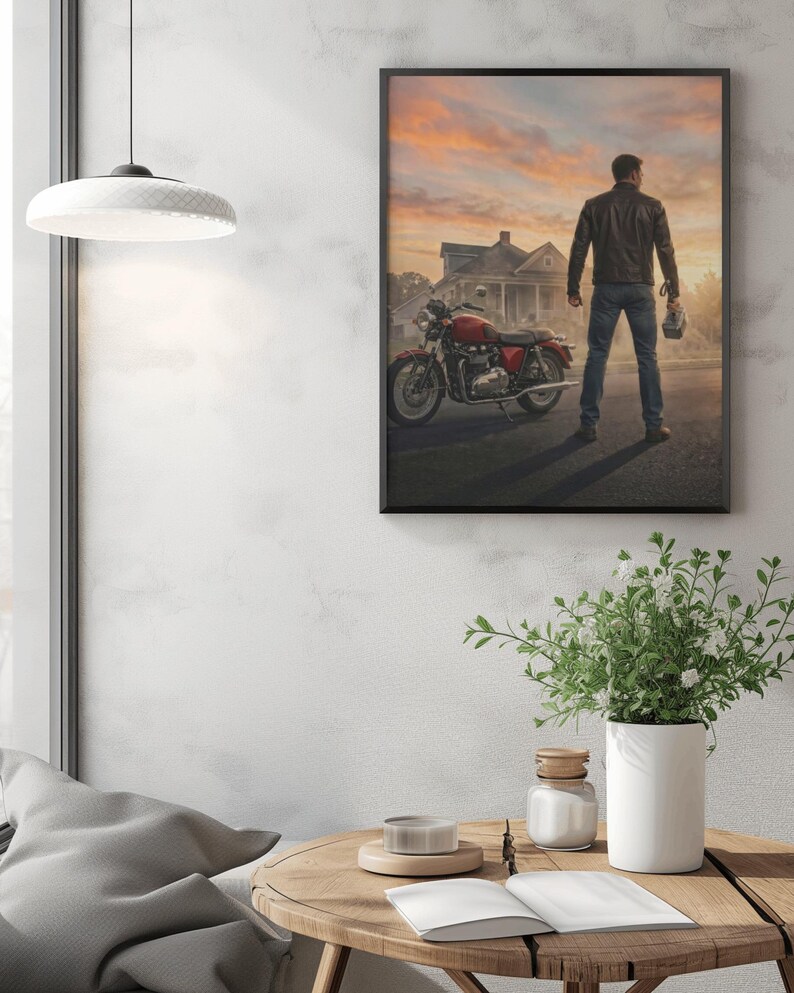 May include: Framed print featuring a man standing next to a red motorcycle, facing away from the viewer. The background shows a house and a sunset sky. The man is wearing a leather jacket and jeans, holding a helmet.