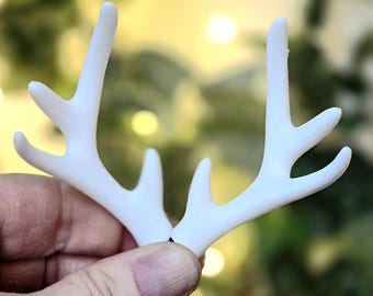 May include: A pair of matte white deer antlers featuring a branched structure with multiple points. The antlers are smooth in texture and display a clean, solid white color throughout, showcasing a realistic shape with curved tines extending upwards.